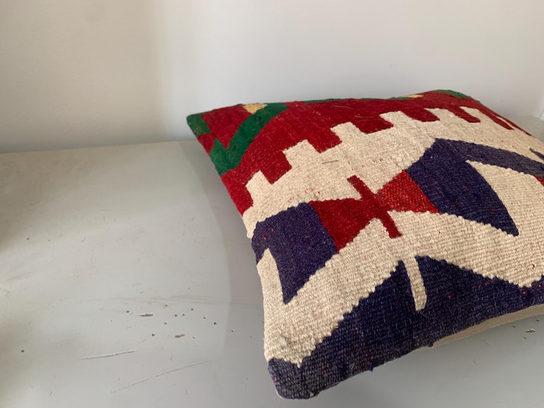 May include: A colorful throw pillow with a geometric pattern in shades of red, green, blue, and white. The pillow is made of woven fabric and has a soft, textured surface.