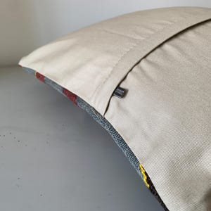 May include: A beige pillow cover with a zipper closure. The pillow cover is made of a soft, textured fabric. The pillow cover is shown on a light gray surface.