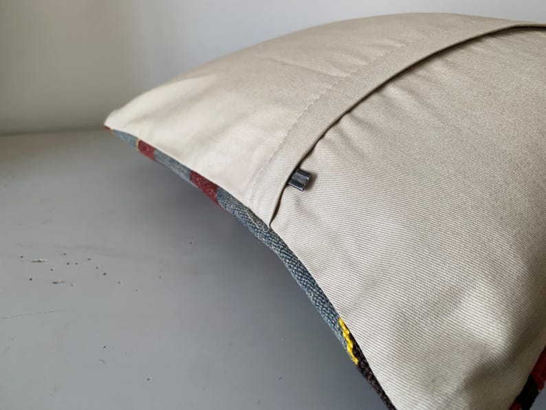 May include: A beige pillow cover with a zipper closure. The pillow cover is made of a soft, textured fabric. The pillow cover is shown on a light gray surface.