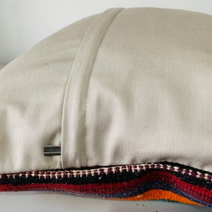 May include: A beige pillow with a zipper closure and a colorful striped fabric on the bottom edge.