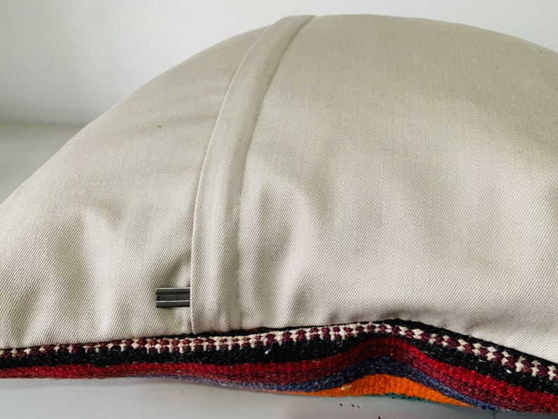 May include: A beige pillow with a zipper closure and a colorful striped fabric on the bottom edge.
