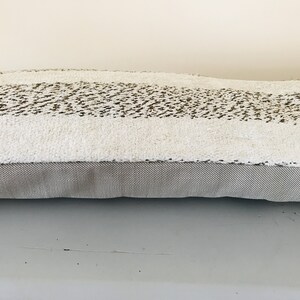 May include: A long, rectangular throw pillow with a white, fluffy fabric and a brown, textured stripe. The pillow has a gray, textured fabric backing.