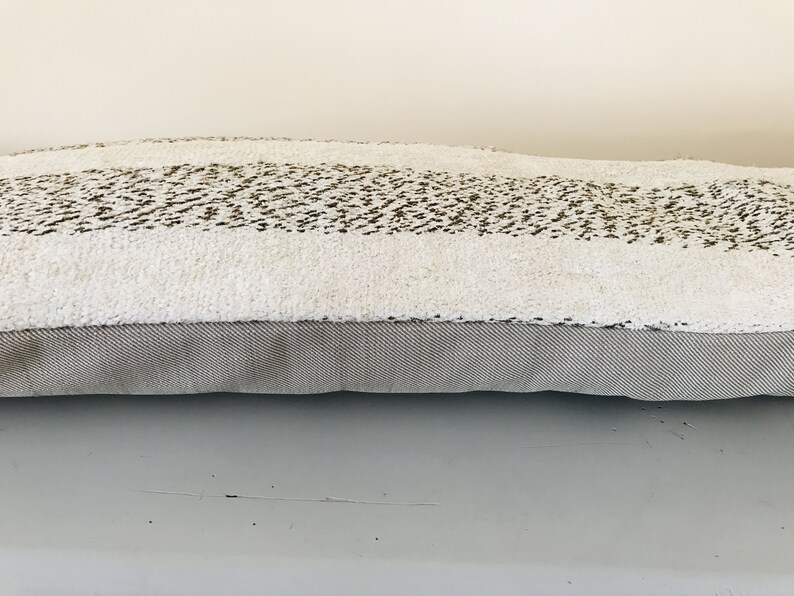 May include: A long, rectangular throw pillow with a white, fluffy fabric and a brown, textured stripe. The pillow has a gray, textured fabric backing.