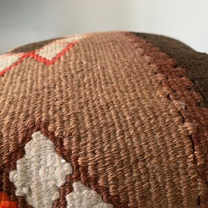May include: A brown, beige, and orange woven pillow with a geometric pattern. The pillow is made of a soft, textured fabric.