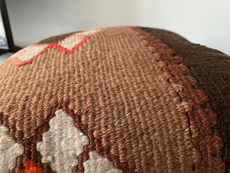 May include: A brown, beige, and orange woven pillow with a geometric pattern. The pillow is made of a soft, textured fabric.