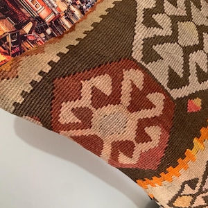 May include: A brown, orange and beige patterned throw pillow with a geometric design. The pillow is made of woven fabric and has a fringed edge.
