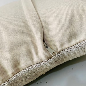 May include: A close-up of a cream-coloured pillow with a zipper closure. The pillow has a textured fabric border.