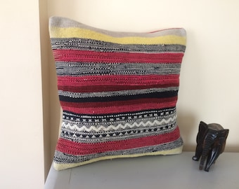 May include: Striped throw pillow with a red, black, white, and yellow color scheme. The pillow has a woven texture and a geometric pattern.