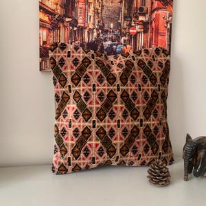 May include: A decorative throw pillow with a geometric pattern in shades of brown, pink, green, and black. The pillow is made of a soft, plush fabric and has a square shape.