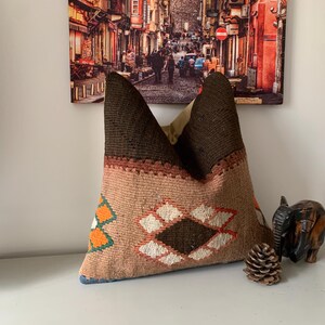 May include: A brown and beige patterned throw pillow with a geometric design. The pillow has a brown and beige color scheme with hints of orange and white.