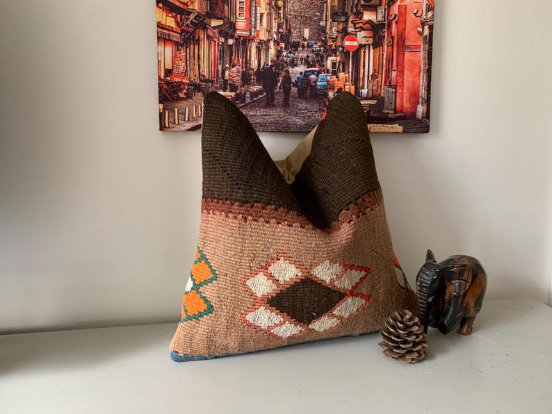 May include: A brown and beige patterned throw pillow with a geometric design. The pillow has a brown and beige color scheme with hints of orange and white.