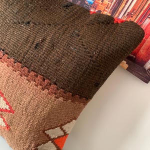 May include: A brown, tan, and orange patterned throw pillow with a geometric design. The pillow is made of a soft, woven fabric.