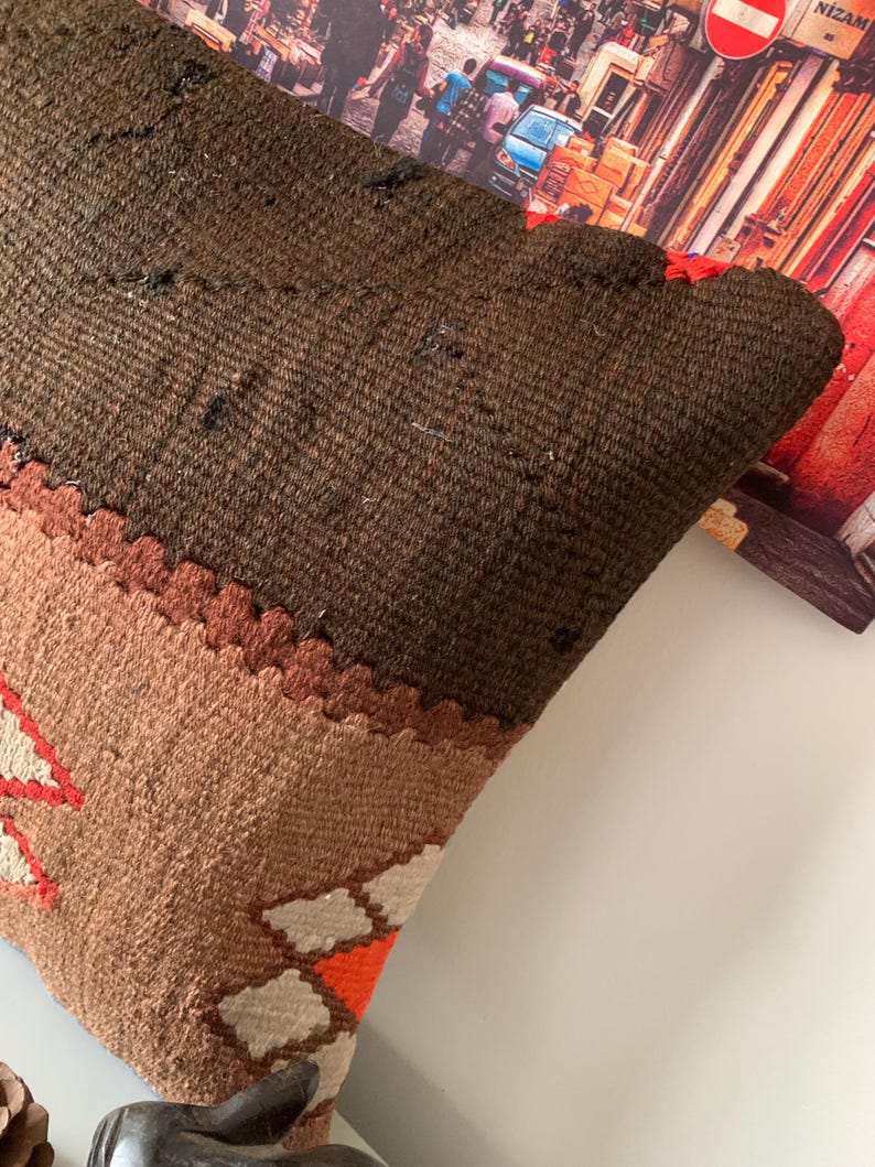 May include: A brown, tan, and orange patterned throw pillow with a geometric design. The pillow is made of a soft, woven fabric.