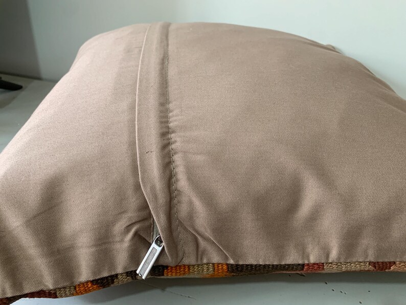 May include: A beige pillow cover with a zipper closure. The cover is made of a soft, textured fabric and has a subtle sheen. The pillow cover is shown folded in half, revealing the zipper and the back side of the fabric.