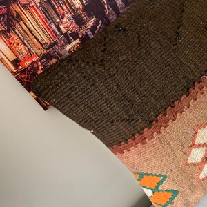 May include: A brown, beige, and orange patterned throw pillow with a geometric design. The pillow is made of woven fabric and has a fringed edge.