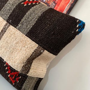 K&ouml;nnte beinhalten: Ein braunes, wei&szlig;es und blaues gestreiftes Kissen mit roten Akzenten. Das Kissen ist aus gewebtem Stoff und hat eine strukturierte Oberfl&auml;che.