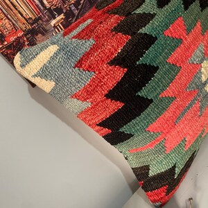 May include: A colorful throw pillow with a geometric pattern in shades of red, blue, green, and black. The pillow is made of woven fabric and has a traditional design.