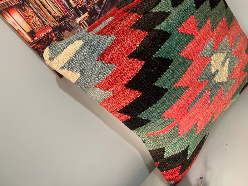 May include: A colorful throw pillow with a geometric pattern in shades of red, blue, green, and black. The pillow is made of woven fabric and has a traditional design.