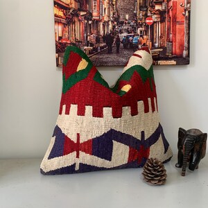 May include: A colorful, handwoven pillow with a geometric pattern in shades of red, green, blue, and white. The pillow is made of a soft, textured fabric and has a unique, bohemian style.