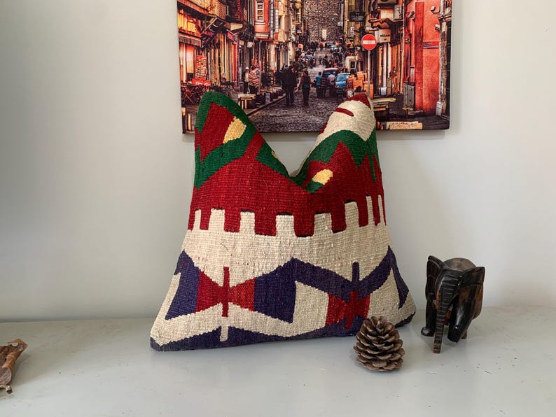 May include: A colorful, handwoven pillow with a geometric pattern in shades of red, green, blue, and white. The pillow is made of a soft, textured fabric and has a unique, bohemian style.