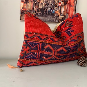 Può includere: Cuscino da lancio rosso, blu e arancione con motivo e frange. Il cuscino è realizzato in tessuto tessuto e presenta un design tradizionale.