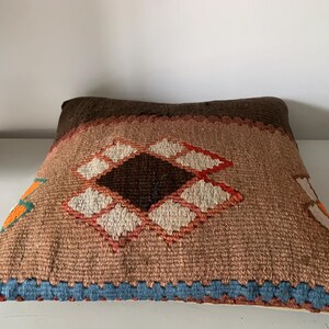 May include: A brown, orange, and white patterned throw pillow with a diamond design. The pillow has a blue fringe around the edges.