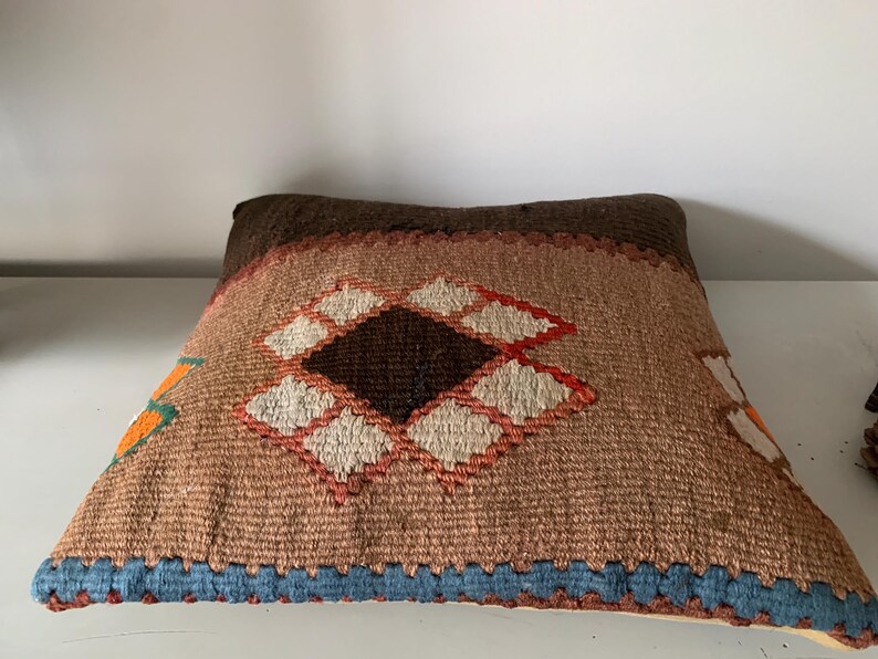 May include: A brown, orange, and white patterned throw pillow with a diamond design. The pillow has a blue fringe around the edges.