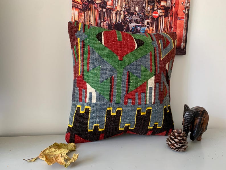 May include: A colorful throw pillow with a geometric pattern in shades of red, green, blue, and black. The pillow is made of woven fabric and has a fringed edge.