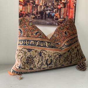May include: A decorative pillow with a floral pattern in shades of pink, blue, and beige. The pillow is made from a woven fabric with a vintage look.