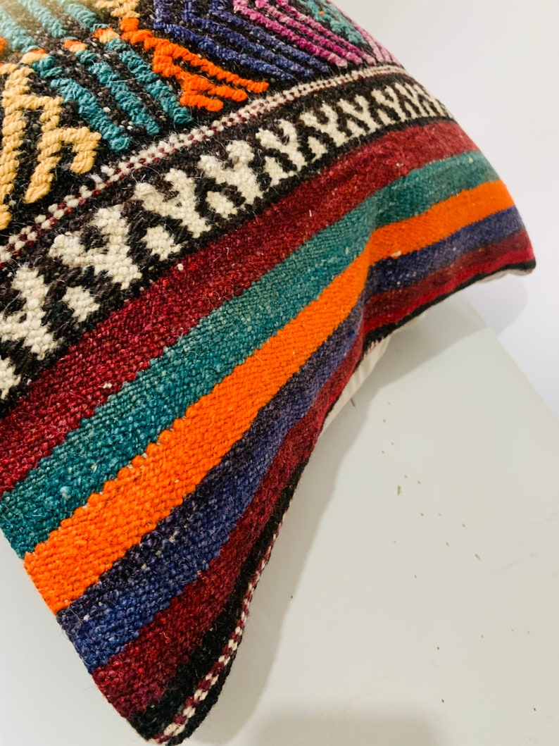 May include: A colorful striped pillow cover with a geometric pattern in the top corner. The pillow cover is made of woven fabric and has a variety of colors, including red, orange, blue, green, and white.