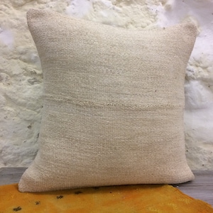 May include: A white, off-white, or cream colored throw pillow with a textured woven fabric. The pillow is sitting on a yellow surface.