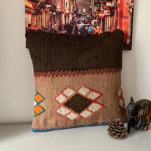 May include: A brown and beige patterned throw pillow with a geometric design. The pillow is made of woven fabric and has a fringe border.