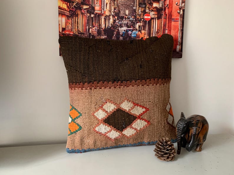 May include: A brown and beige patterned throw pillow with a geometric design. The pillow is made of woven fabric and has a fringe border.
