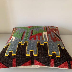 May include: A colorful, geometric patterned throw pillow with a blue, green, red, black, and yellow design. The pillow is made of woven fabric and has a white backing.
