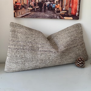 May include: A large, rectangular pillow with a textured, neutral-toned fabric. The pillow has dark brown horizontal stripes and is displayed with a wooden elephant figurine and a pinecone. Decorative home decor.
