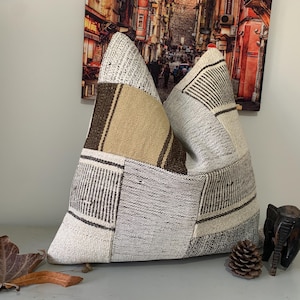 May include: A patchwork cushion with brown and beige stripes and a white background. The cushion is made of woven fabric and has a textured surface.