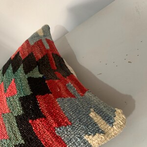 May include: A colorful throw pillow with a geometric pattern in shades of red, blue, green, and black. The pillow is made of a woven fabric and has a soft, textured surface.