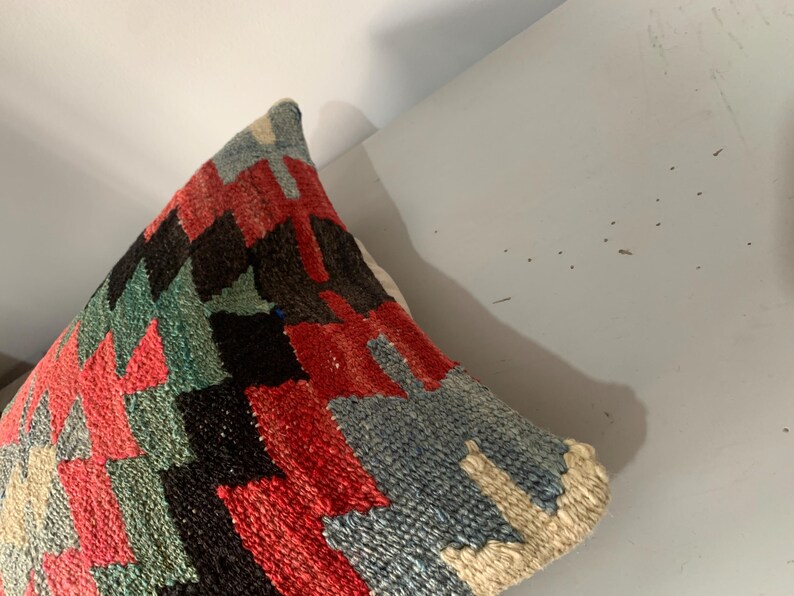 May include: A colorful throw pillow with a geometric pattern in shades of red, blue, green, and black. The pillow is made of a woven fabric and has a soft, textured surface.