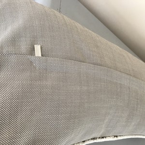 May include: A beige pillow with a zipper closure on the back. The pillow is made of a textured fabric with a subtle diagonal pattern.