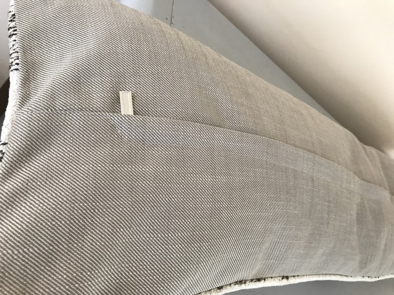 May include: A beige pillow with a zipper closure on the back. The pillow is made of a textured fabric with a subtle diagonal pattern.
