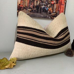 May include: A white pillow with brown and beige stripes. The pillow is made of a woven fabric and has a soft, textured surface.