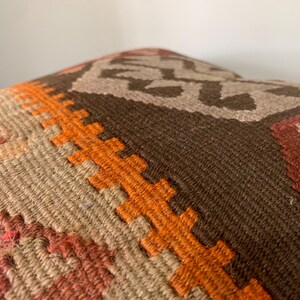 May include: A close-up of a brown, orange and beige patterned throw pillow. The pillow is made of woven fabric with a geometric design.
