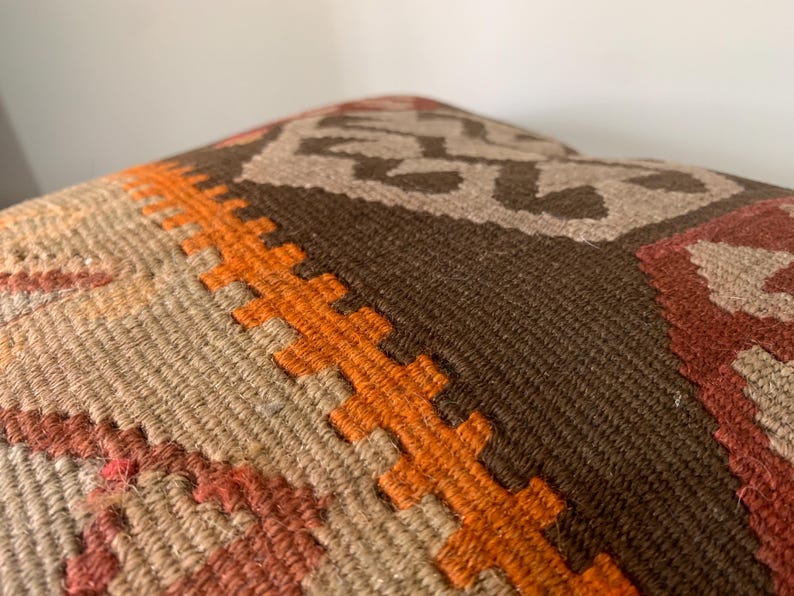 May include: A close-up of a brown, orange and beige patterned throw pillow. The pillow is made of woven fabric with a geometric design.