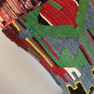 May include: A colorful throw pillow with a geometric pattern in shades of red, green, blue, yellow, and black. The pillow is made of woven fabric and has a textured surface.