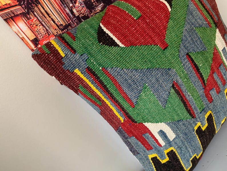May include: A colorful throw pillow with a geometric pattern in shades of red, green, blue, yellow, and black. The pillow is made of woven fabric and has a textured surface.