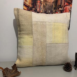 May include: A patchwork pillow cover with beige and yellow squares. The pillow cover is made of a soft, textured fabric.