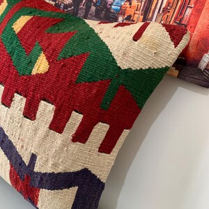 May include: A colorful throw pillow with a geometric pattern in shades of red, green, white, and blue. The pillow is made of woven fabric and has a textured surface.