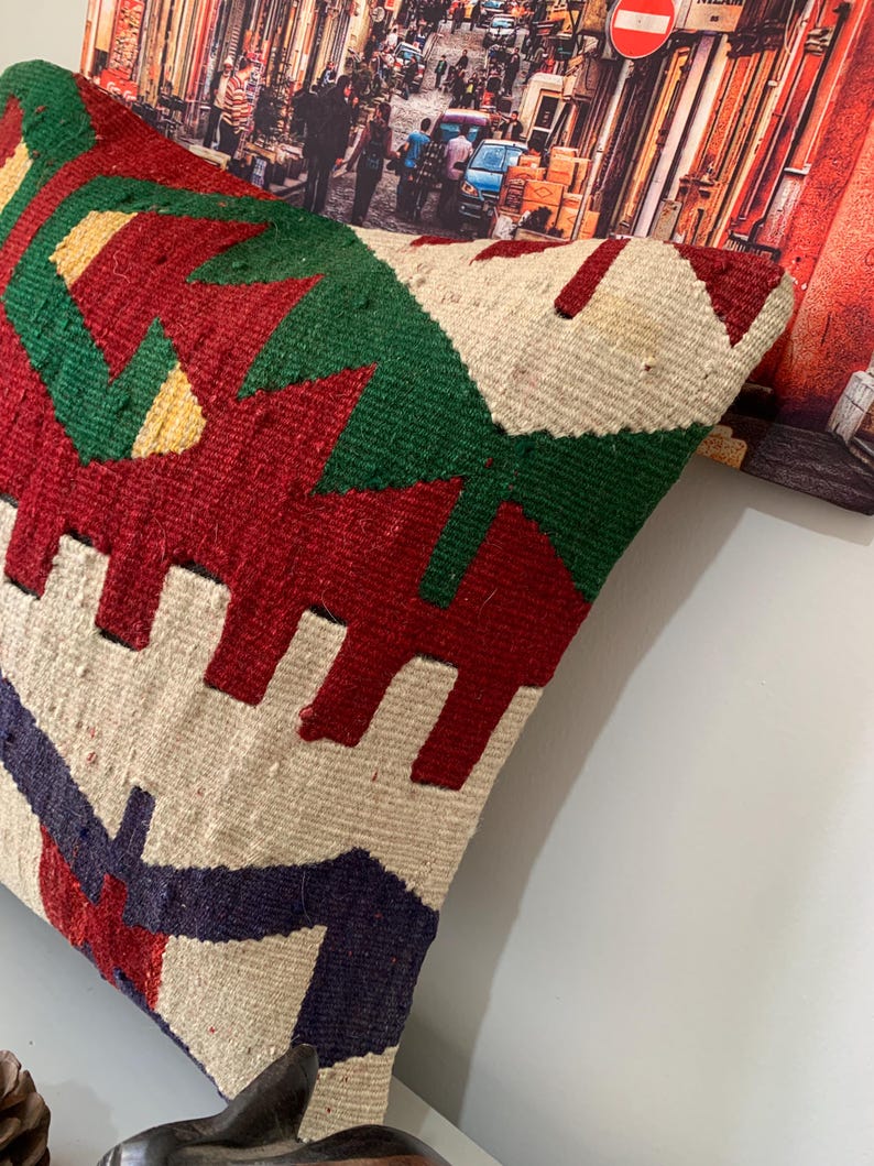 May include: A colorful throw pillow with a geometric pattern in shades of red, green, white, and blue. The pillow is made of woven fabric and has a textured surface.