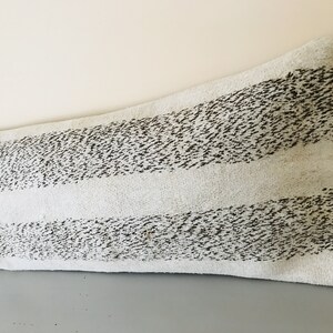 May include: A long, white lumbar pillow with black stripes. The pillow has a textured, fuzzy surface.