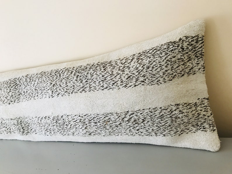 May include: A long, white lumbar pillow with black stripes. The pillow has a textured, fuzzy surface.